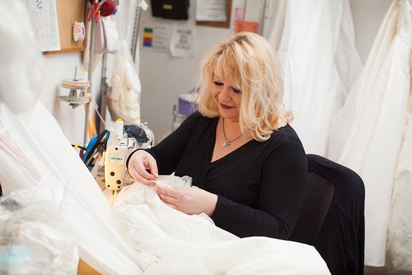 Seamstress Alena Lipovsky hand stitches alterations on a bridal gown. Photo credit: Topher Stevenson / J Thomas Photography