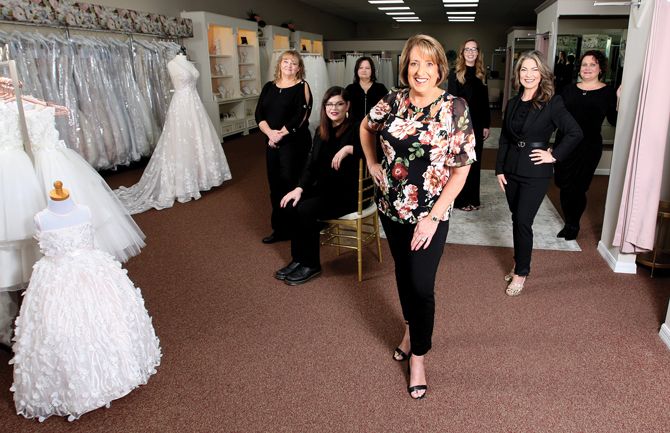 The Aurora Bridal team: Cami Hester, owner (front); Casey Stains, stylist (sitting); Annette Gaston, alterations manager (standing to the side of Casey); 
Linda Goldsborough, alterations assistant (standing behind Casey); Trista Stokrocki, stylist (over Cami’s shoulder); Roxi Ris, stylist (touching the wall);
Heather Didion, lead stylist (hand on hip).